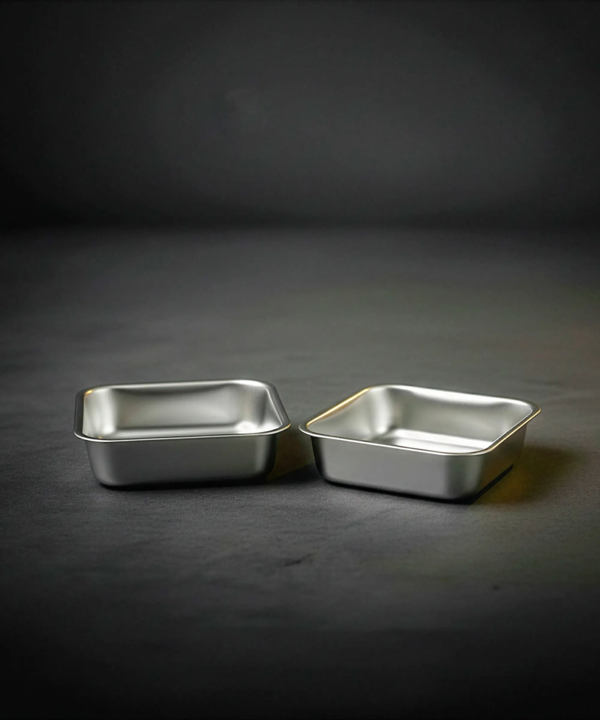 Two metallic baking trays on a dark gray background